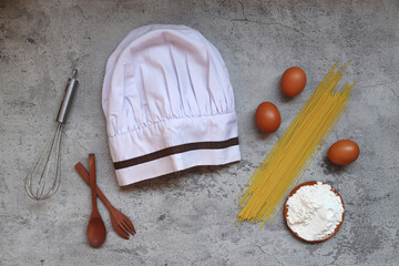 Top view of chef hat with cooking ingredients on grey rustic background