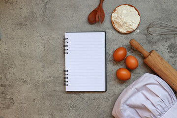 Top view of blank recipe notes with chef hat and cooking ingredients on grey rustic background