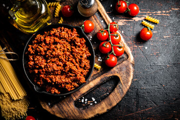 Bolognese sauce on a cutting board with cherry tomatoes and dry pasta. 