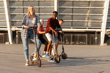 interracial group of young friends ride electric scooters in the city, multiracial youth use...