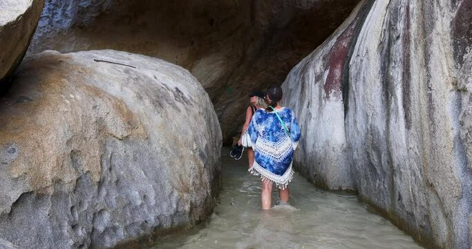 Virgin Gorda Caribbean ocean Baths rocks women wading cave 4K. British Virgin Islands. Christopher Columbus discovered the island. Cruise ship vacation destination. Yacht, sailboat harbor marina. 