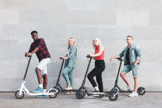 interracial company of friends rides electric scooters against the background of a wall, people use eco transport in the city