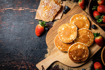 Pancakes on a wooden cutting board with honey and berries.