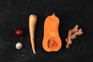 Raw butternut squash with red onion, ginger, parsnip and garlic on black background. Pumpkin soup...