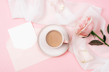 A coffee cup, pink rose and envelope with blank card. Holiday concept. Top view, flat lay, mockup