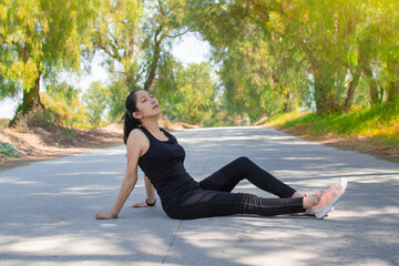 Mujer delgada con ropa de ejercicio fitness recostada en el asfalto de una carretera en la...