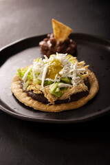 Sopes de Pollo. Traditional homemade Mexican appetizer prepared with fried corn dough covered with refried beans, green or red sauce, lettuce, cheese, onion and shredded chicken