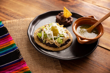 Sopes de Pollo. Traditional homemade Mexican appetizer prepared with fried corn dough covered with refried beans, green or red sauce, lettuce, cheese, onion and shredded chicken