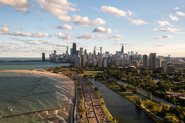 Downtown Chicago city skyline aerial centered over traffic along Lake Shore Drive between South Lagoon and Lake Michigan on a sunny day with fluffy white clouds in a blue sky above.