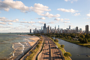 Downtown Chicago city skyline aerial centered over traffic along Lake Shore Drive between South Lagoon and Lake Michigan on a sunny day with fluffy white clouds in a blue sky above.