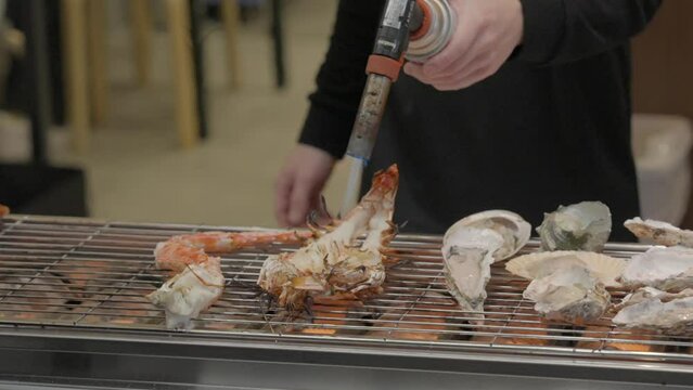 This close up video shows a street food vendor's hands using a torch to cook lobster seafood in slow motion.