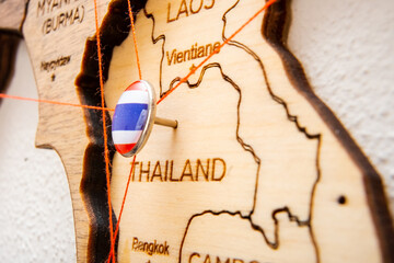 Thailand flag on the pushpin with red thread showed the paths of movement or areas of influence in the global economy on the wooden map. Planning of traveling or logistic concept. Network connection. 