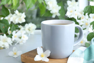 Cup of tea and fresh jasmine flowers on light grey table