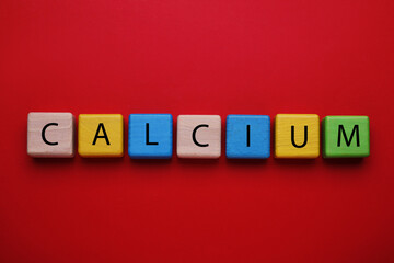 Word Calcium made of colorful wooden cubes with letters on red background, flat lay