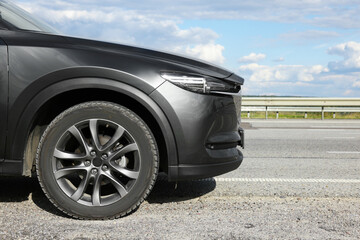 New black modern car on asphalt road, closeup. Space for text