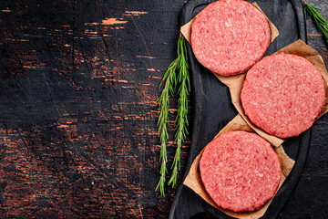 Raw burger on a cutting board with rosemary.