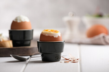 Fresh soft boiled egg in cup served on white wooden table. Space for text