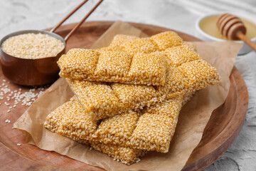 Wooden tray with delicious sweet kozinaki bars and sesame seeds on white table, closeup