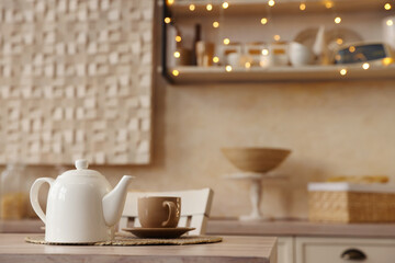 White teapot with cup on wooden table in kitchen, space for text