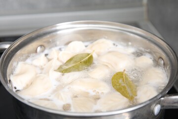 Cooking dumplings (varenyky) with tasty filling and bay leaves in pot indoors, closeup