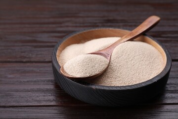 Bowl and spoon with active dry yeast on wooden table, closeup. Space for text