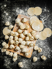 Raw dumplings and round pieces of dough on a cutting board. 