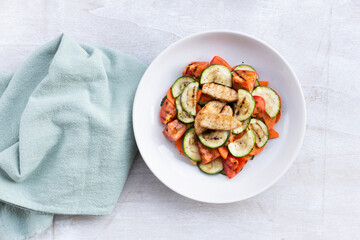 Healthy food grilled chicken salad has zucchini carrot tomato in white bowl on wood background.