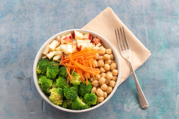 Healthy food broccoli salad add apple chickpeas in white bowl on blue wood background.