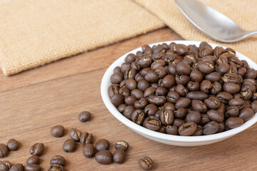 medium roasted peaberry coffee beans in a ceramic dish on wooden table, close up.