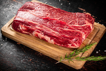 Raw beef on a wooden cutting board with rosemary.
