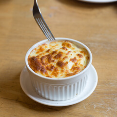 Fork is scooping up cheese mashed potatoes in white cup on the wood table in restaurant