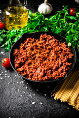 Bolognese sauce in a frying pan with pasta dry and parsley. 