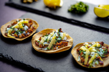 Delicious lunch with tacos and sauces on black table of appetizing Mexican tacos served on black plate near bowl with tomato sauce and avocado placed on wooden table