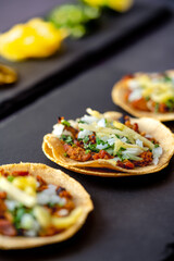 Delicious lunch with tacos and sauces on black table of appetizing Mexican tacos served on black plate near bowl with tomato sauce and avocado placed on wooden table