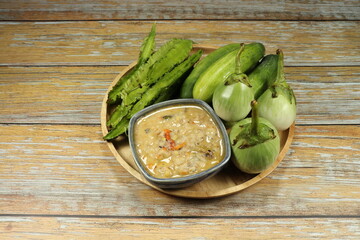 Spicy fish dipping sauce serving with fresh vegetable serving on the wooden plate. Famous spicy starter menu in Thai restaurant. 
