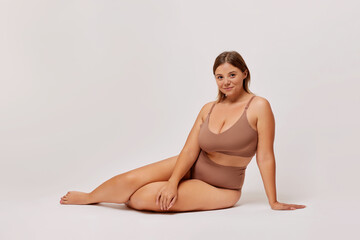 Plus size self enjoyed woman wearing lingerie sitting on a floor isolated over white background....