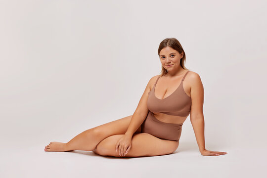 Plus size self enjoyed woman wearing lingerie sitting on a floor isolated over white background. Body Positive concept
