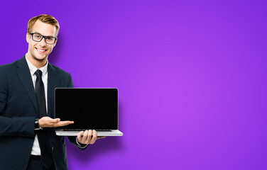 Business man in glasses spectacles, black suit showing laptop with empty mockup screen, on violet purple background, with copy space. It expert,  technician repair service, tech support, maintenance.