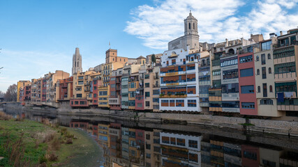 Fototapeta na wymiar Colorful houses reflected in the Onyar river, in Girona, Catalonia, Spain. Church of Sant Feliu and Cathedral of Santa María in the background