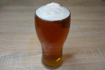 A glass of amber beer with thick white beer foam on a wooden table                     