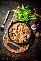 Liver in a frying pan on a cutting board with parsley and spices. 