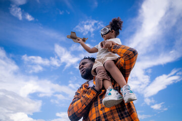 Happy African American father engineer carrying his daughter with a blue sky background. Cheerful father carrying daughter on shoulders outdoor.