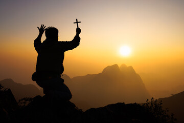 Silhouette of christian man praying with a  cross at sunrise, Christian Religion concept background.