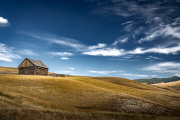 A small log cabin on a hillside under a deep blue sky along the Alberta Foothills near Pincher Creek Canada.