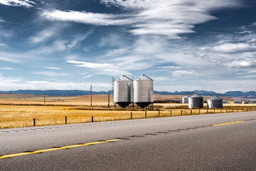 Pair of steel grain silos standing next to a divided highway along harvested fields and distant Rocky Mountains at background near Longview Alberta Canada.. © Ramon Cliff