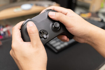 Black game controller with hand. The man's hands hold the console controller in the foreground. Playing video games at home.
