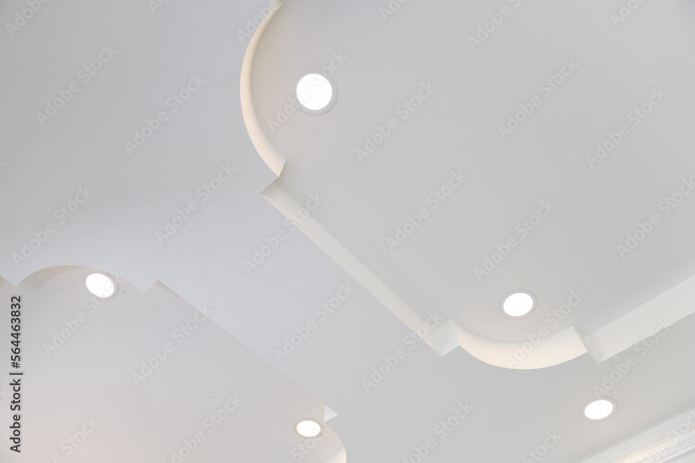 Poster stretch ceiling white and complex shape. ceiling with halogen spots lamps and drywall construction i