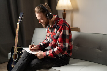 Pensive man composer, musician writing song and playing guitar on sofa in the evening.