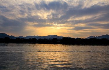 Fototapeta premium A calm seascape with mountains at sunset. Dramatic sky and cloudscape. For travel, background and blog etc. concepts. West Lake. Popular park of Hangzhou city China