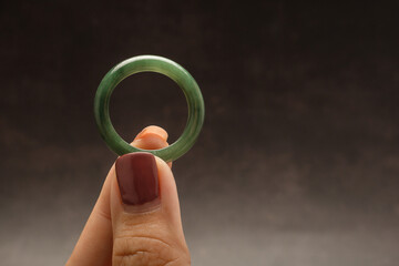 Hand holding of a green jade ring on a black background